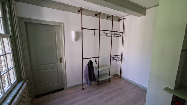 Steigerbuis kapstok met koperen buizen en twee verstelbare houten schappen en vele horizontale buizen om kleerhangers aan op te hangen.