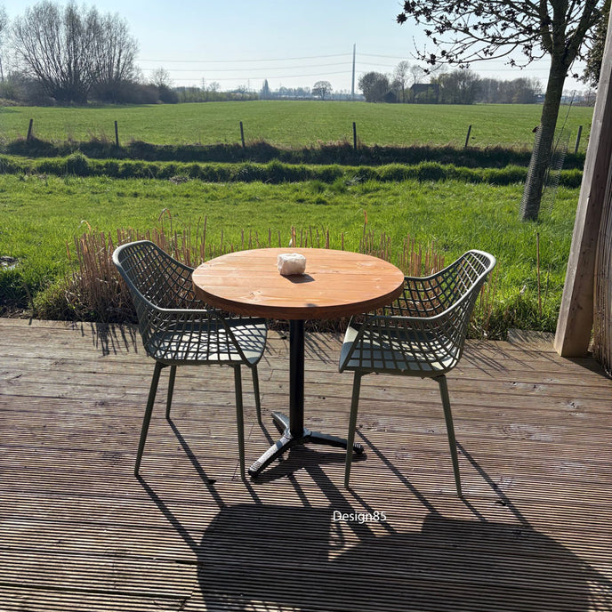 Compacte horecatafel voor buiten met warm houten tafelblad, twee groene rasterstoelen en een natuurlijke bamboeschutting op de achtergrond.