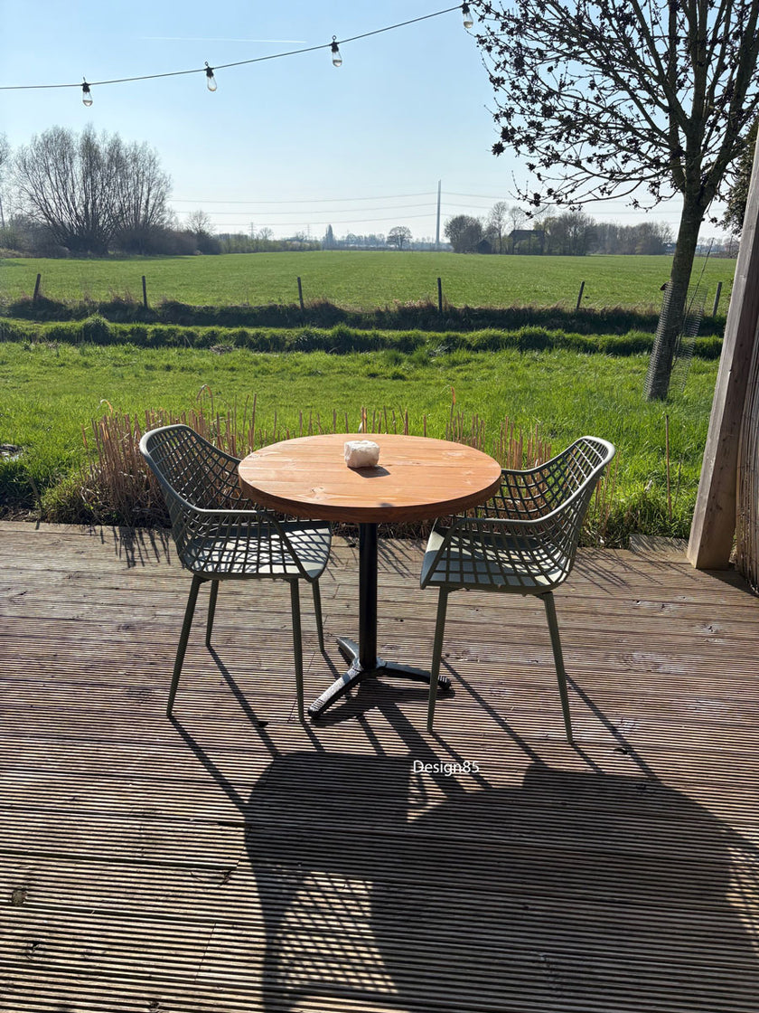 Compacte horecatafel voor buiten met warm houten tafelblad, twee groene rasterstoelen en een natuurlijke bamboeschutting op de achtergrond.