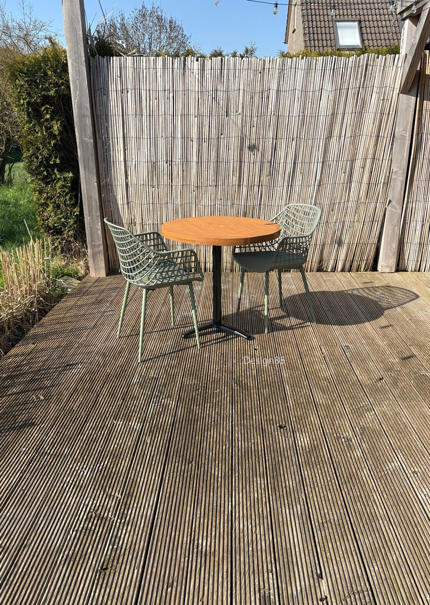 Terrasmeubelset met compacte ronde tafel, zwart onderstel en twee groene stoelen op een houten vlonder in de tuin.