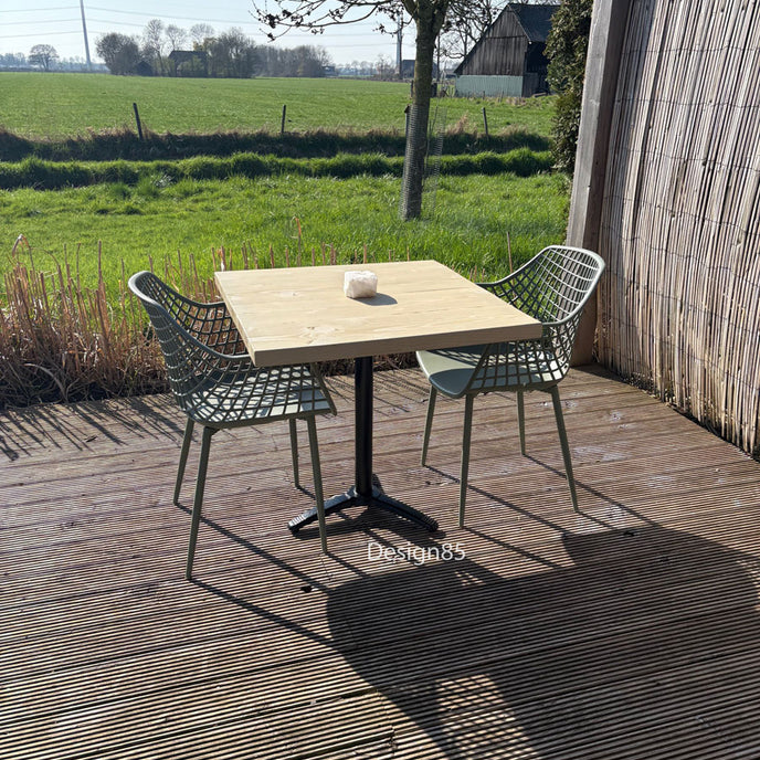 Industriële bartafel met houten blad op een terras in de tuin, omringd door planten en moderne stoelen.