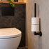 Industriële WC Rolhouder van zwart staal met twee toiletrollen, aan de muur gemonteerd naast een modern wit toilet in een stijlvolle badkamer.