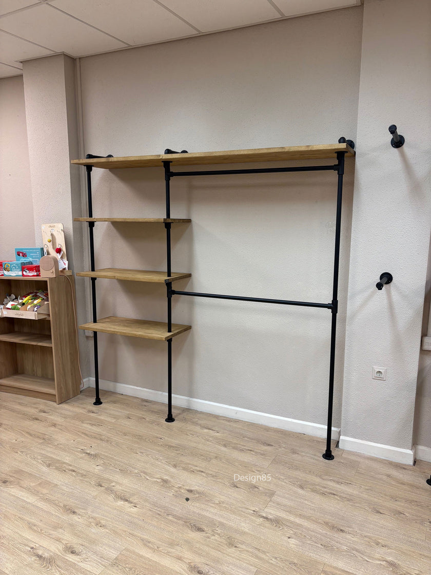 Industrieel kledingrek voor kinderen aan de muur met houten legplanken en zwart stalen frame in een lichte ruimte.