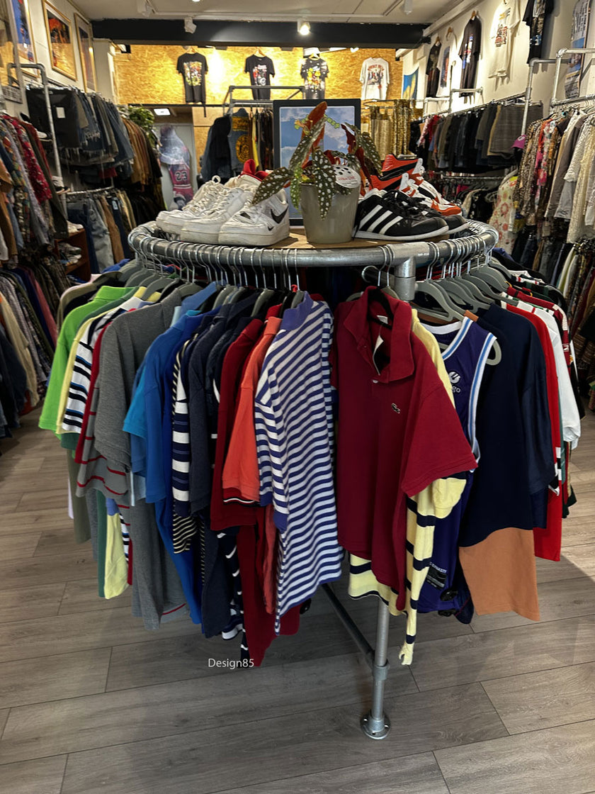 Rond steigerbuis kledingrek met kleding en sneakers in een moderne vintage kledingwinkel.