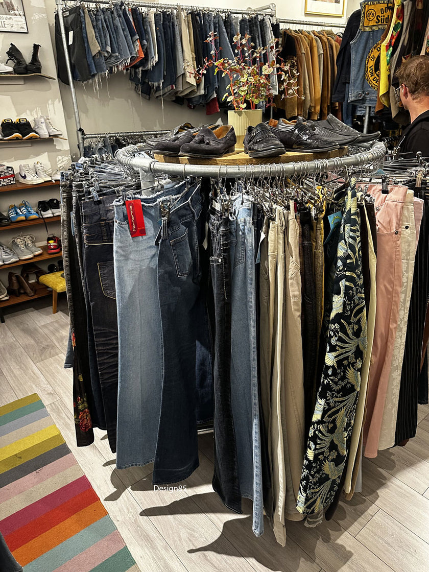 Steigerbuis kledingrek rond model met houten bovenblad en kleding rondom opgesteld in een winkelinterieur.