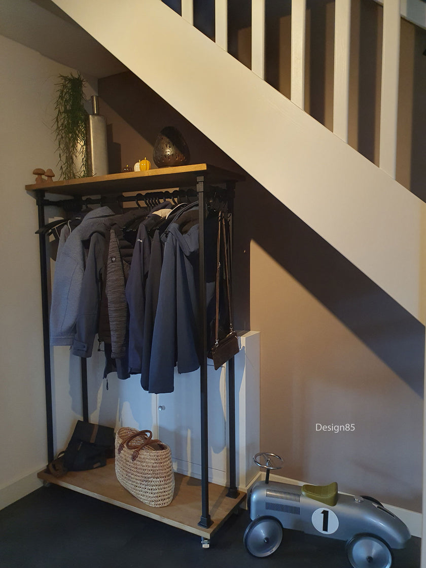 steigerbuis kledingrek vierkant met zwarte kokers en met vurenhout in het bruin. Het kledingrek staat onder een trap.