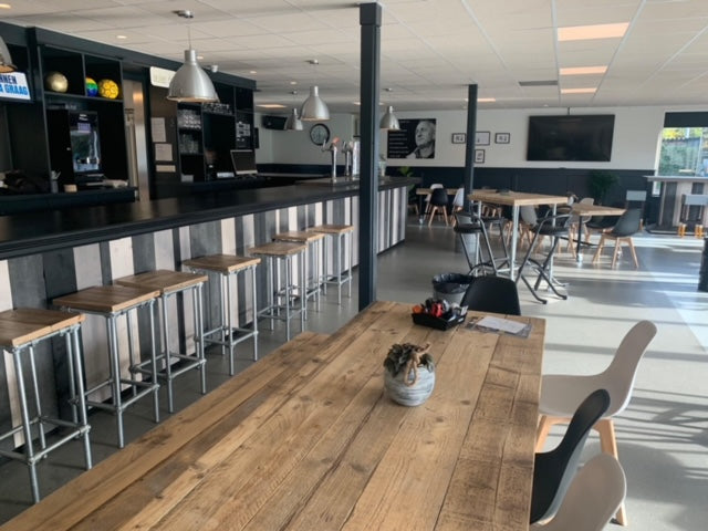 Tafel van steigerbuizen met gebruikt steigerhout en zwart metalen frame in een sportkantine.
